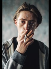 Jongeman met een LVB en een verslaving kijkt in de camera terwijl hij aan het roken is. 