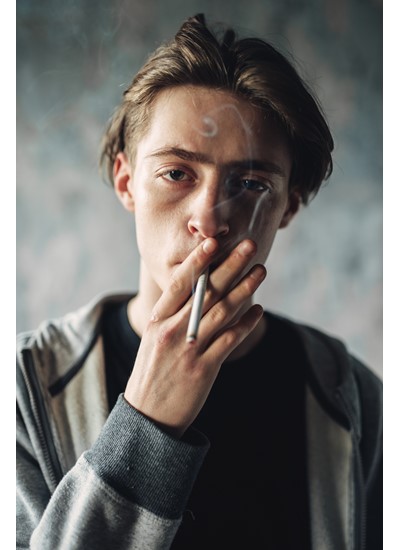 Jongeman met een LVB en een verslaving kijkt in de camera terwijl hij aan het roken is. 